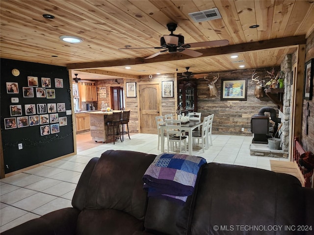 living area with light tile patterned floors, visible vents, wood ceiling, a wood stove, and beam ceiling