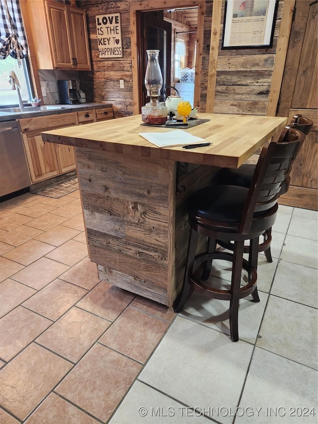 bar featuring a sink, wood walls, light tile patterned floors, and stainless steel dishwasher