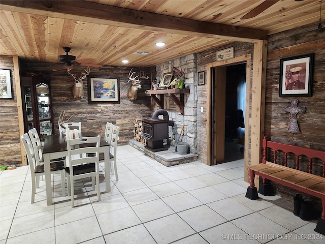 dining space featuring light tile patterned floors, a ceiling fan, a wood stove, wooden ceiling, and beamed ceiling