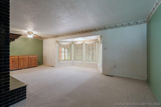 unfurnished room with a textured ceiling, light colored carpet, and brick wall