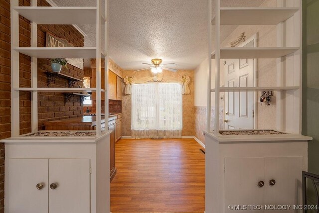 kitchen with ceiling fan, light hardwood / wood-style flooring, a textured ceiling, and brick wall