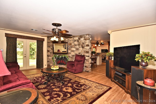 living room with light wood-type flooring, a stone fireplace, ceiling fan, and french doors