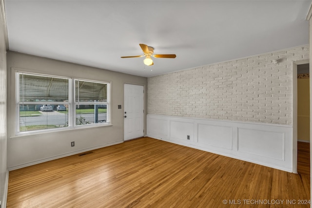 unfurnished room featuring light hardwood / wood-style floors, brick wall, and ceiling fan