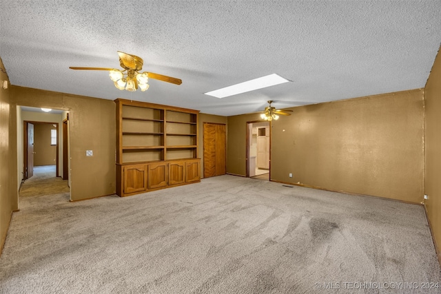 carpeted empty room featuring ceiling fan, a skylight, a textured ceiling, and built in shelves