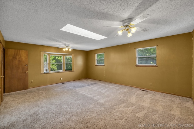 carpeted spare room with ceiling fan, a textured ceiling, and a skylight