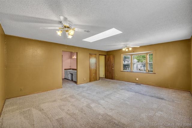 carpeted spare room with ceiling fan, a textured ceiling, and a skylight