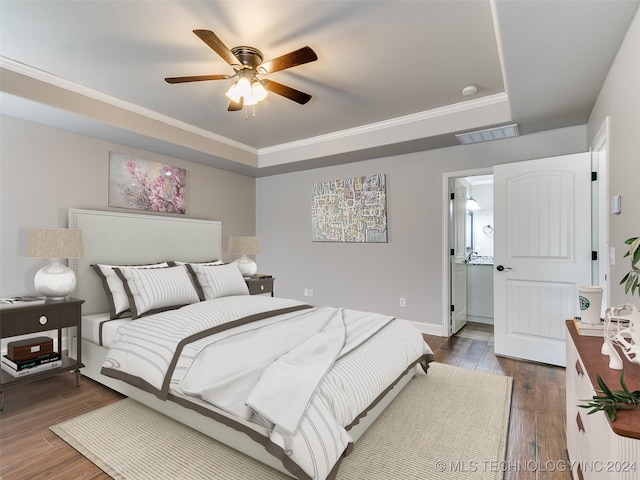 bedroom with ceiling fan, a tray ceiling, hardwood / wood-style floors, ensuite bathroom, and crown molding