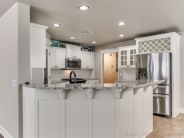 kitchen with tasteful backsplash, appliances with stainless steel finishes, light stone counters, light tile patterned floors, and kitchen peninsula