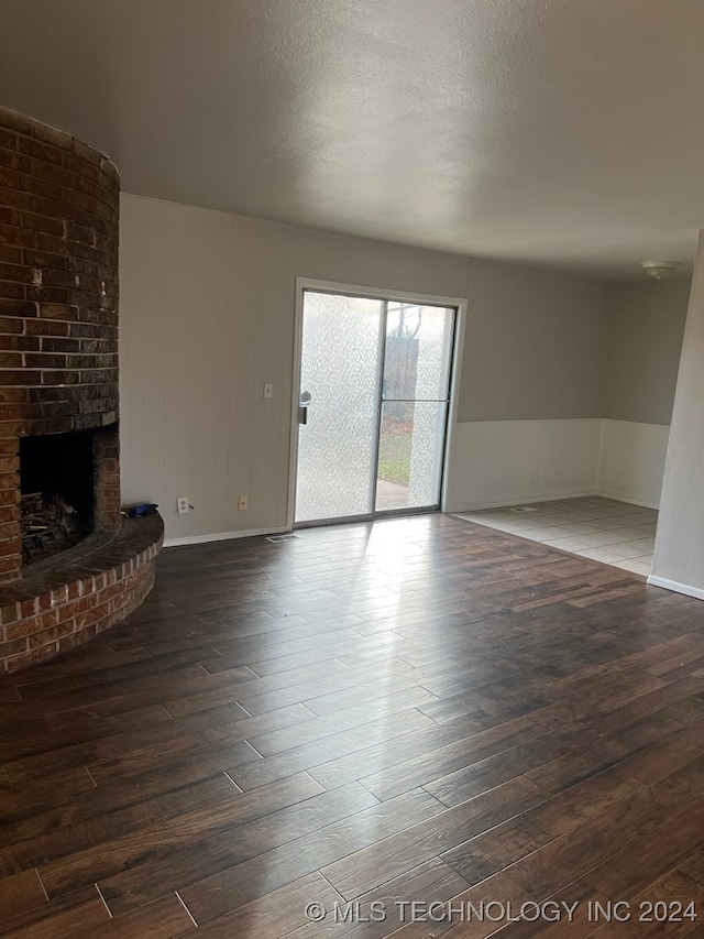 unfurnished living room featuring hardwood / wood-style floors, brick wall, a textured ceiling, and a fireplace