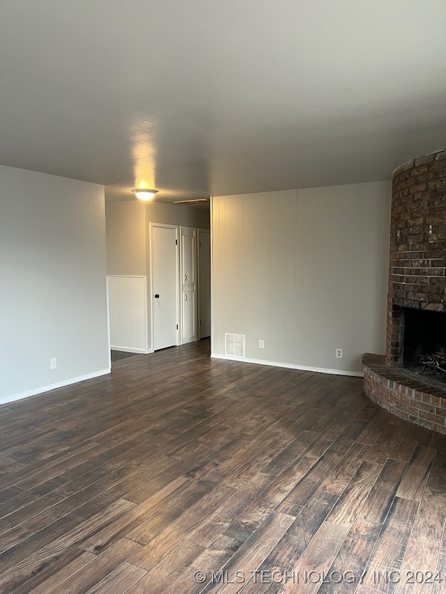 unfurnished living room with dark hardwood / wood-style flooring, a fireplace, and brick wall