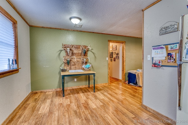 corridor with a textured ceiling, light hardwood / wood-style flooring, and crown molding