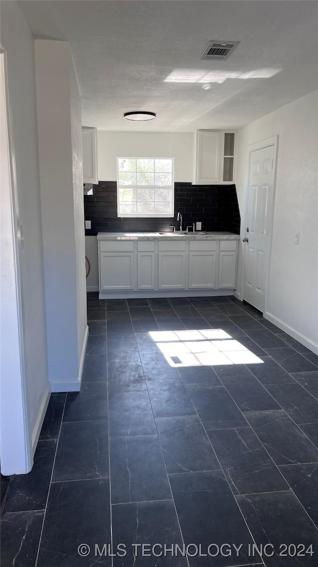 kitchen with tasteful backsplash, visible vents, white cabinetry, a sink, and baseboards