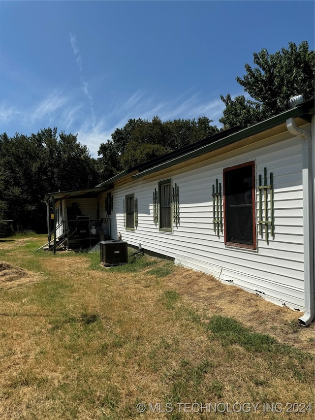 view of side of home with central AC unit and a yard