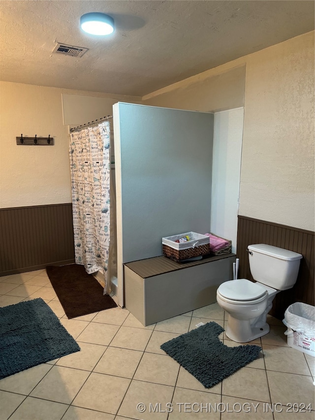 bathroom with a textured ceiling, curtained shower, toilet, and tile patterned floors