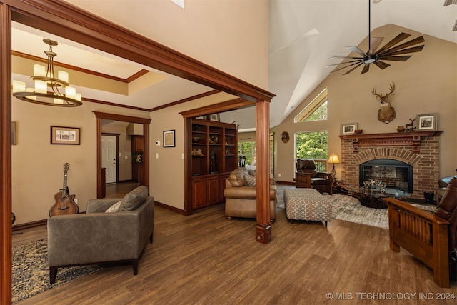 living room featuring crown molding, vaulted ceiling, a brick fireplace, dark hardwood / wood-style flooring, and ceiling fan with notable chandelier