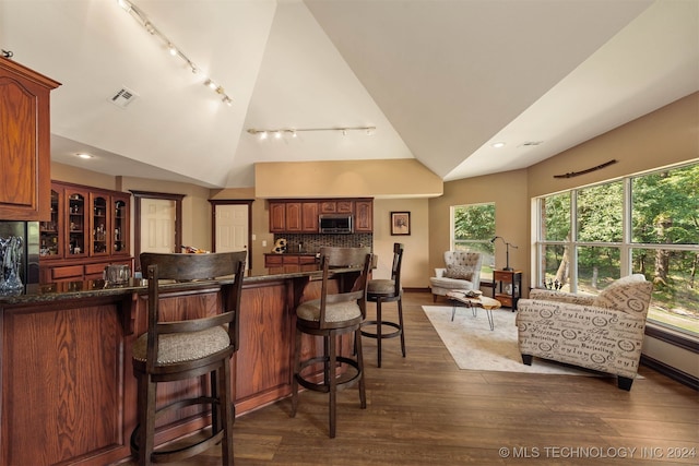 kitchen with dark wood-type flooring, a kitchen bar, high vaulted ceiling, black fridge, and decorative backsplash