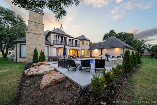 back house at dusk featuring a patio area, an outdoor hangout area, a balcony, and a lawn