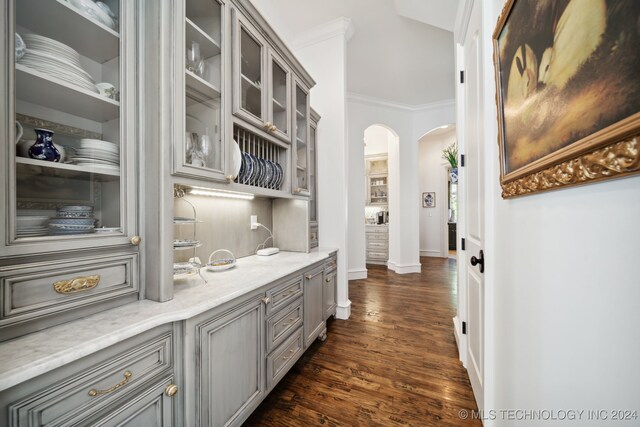 bar with dark hardwood / wood-style flooring, decorative backsplash, light stone countertops, crown molding, and gray cabinets