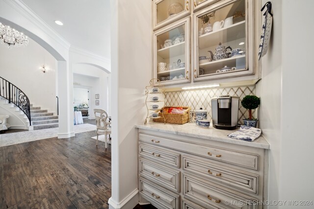 bar featuring tasteful backsplash, hardwood / wood-style floors, cream cabinets, light stone countertops, and crown molding