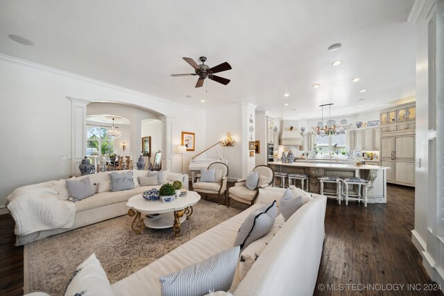 living room featuring ceiling fan with notable chandelier, decorative columns, dark hardwood / wood-style floors, and ornamental molding