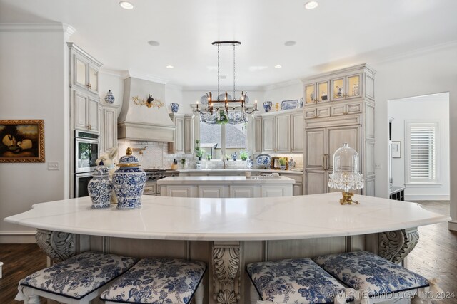 kitchen featuring a spacious island, decorative light fixtures, a breakfast bar area, and custom range hood