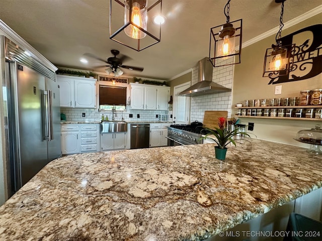 kitchen featuring wall chimney range hood, white cabinets, sink, decorative light fixtures, and premium appliances