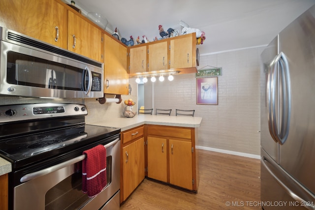 kitchen with brick wall, appliances with stainless steel finishes, kitchen peninsula, and light hardwood / wood-style flooring