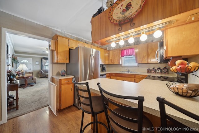 kitchen with a breakfast bar, sink, kitchen peninsula, stainless steel appliances, and light wood-type flooring