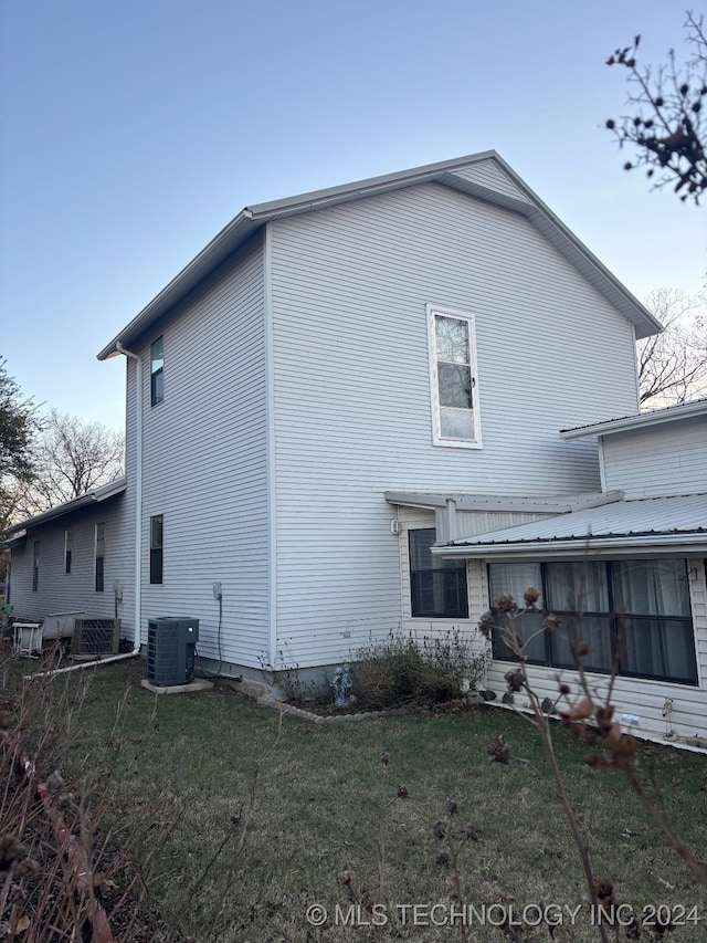 back of house featuring central air condition unit and a lawn