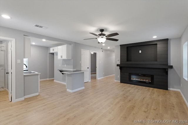 unfurnished living room featuring sink, light hardwood / wood-style flooring, ceiling fan, and a large fireplace