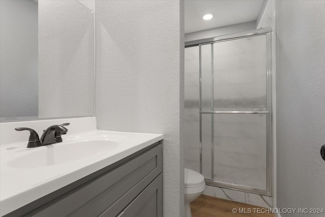 bathroom with hardwood / wood-style floors, toilet, vanity, and a shower with shower door