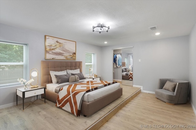 bedroom featuring light wood-type flooring, a spacious closet, a closet, and a textured ceiling