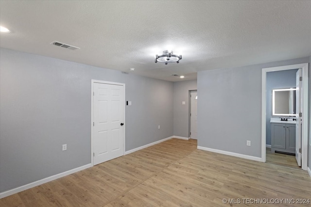 unfurnished room with sink, a textured ceiling, and light hardwood / wood-style floors