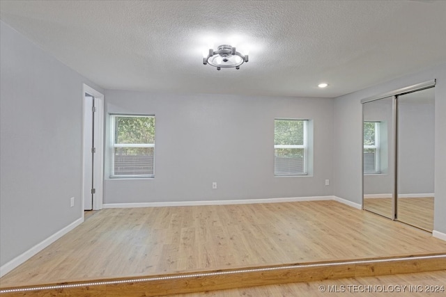 unfurnished bedroom featuring light wood-type flooring, a closet, a textured ceiling, and multiple windows