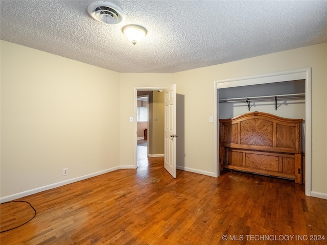 unfurnished bedroom with wood-type flooring, a textured ceiling, and a closet