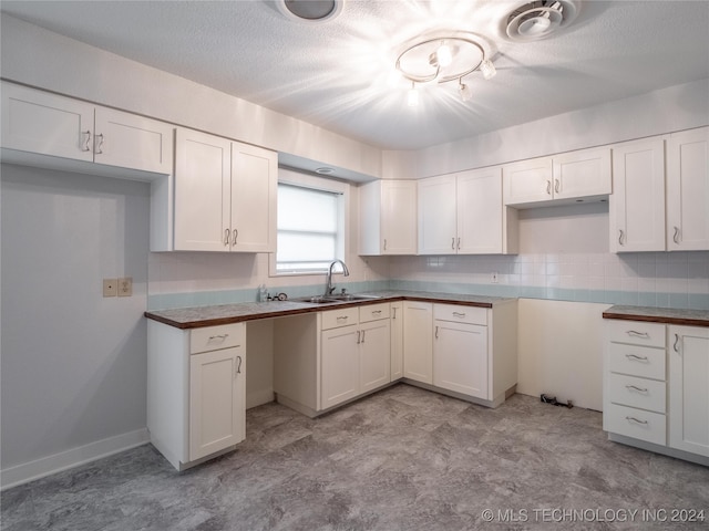 kitchen with a textured ceiling, white cabinetry, and sink