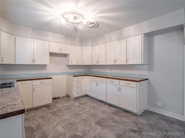 kitchen with a textured ceiling, backsplash, white cabinetry, and sink