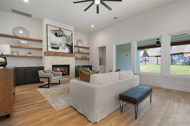 living room with built in shelves, a brick fireplace, light hardwood / wood-style flooring, and ceiling fan