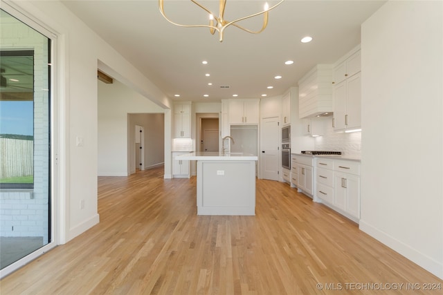 kitchen with white cabinetry, sink, light hardwood / wood-style flooring, and a center island with sink