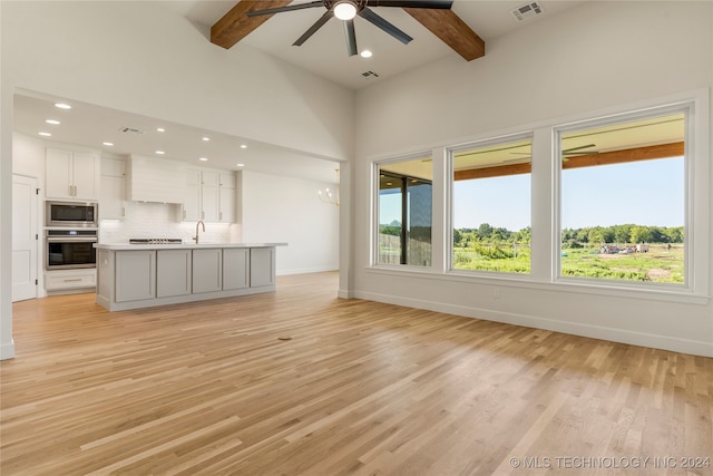 unfurnished living room with sink, beam ceiling, light hardwood / wood-style flooring, and a healthy amount of sunlight