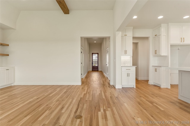 unfurnished living room with beam ceiling, a high ceiling, and light hardwood / wood-style flooring