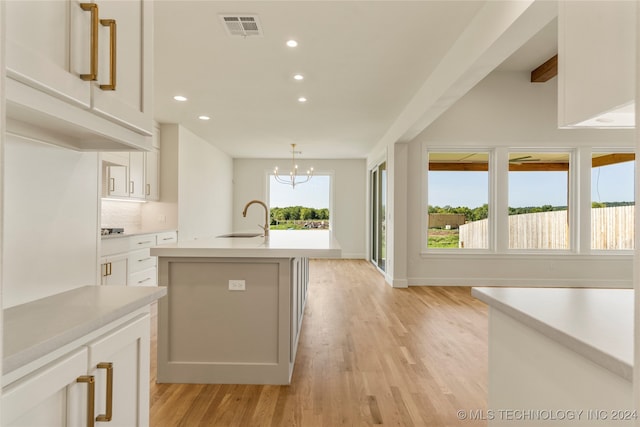 kitchen with light wood-type flooring, pendant lighting, white cabinetry, sink, and a center island with sink