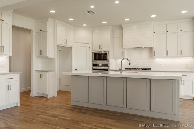 kitchen featuring stainless steel appliances, an island with sink, and light hardwood / wood-style flooring