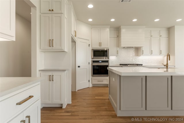 kitchen with appliances with stainless steel finishes, tasteful backsplash, light wood-type flooring, white cabinets, and custom exhaust hood