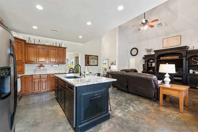 kitchen with light stone countertops, sink, tasteful backsplash, stainless steel refrigerator with ice dispenser, and a kitchen island with sink