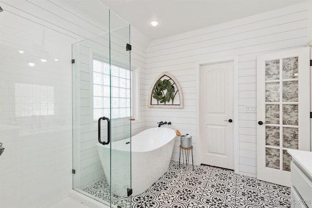 bathroom featuring plus walk in shower, vanity, wood walls, and tile patterned flooring