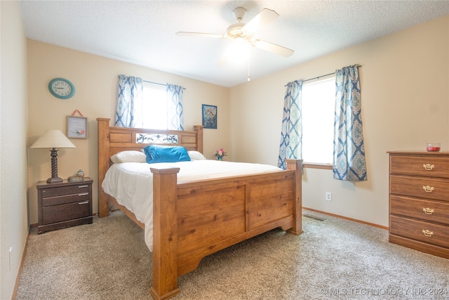 bedroom with ceiling fan, light colored carpet, and a textured ceiling