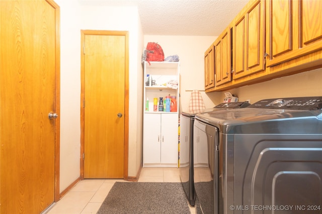 laundry area featuring a textured ceiling, light tile patterned floors, cabinets, and washing machine and clothes dryer