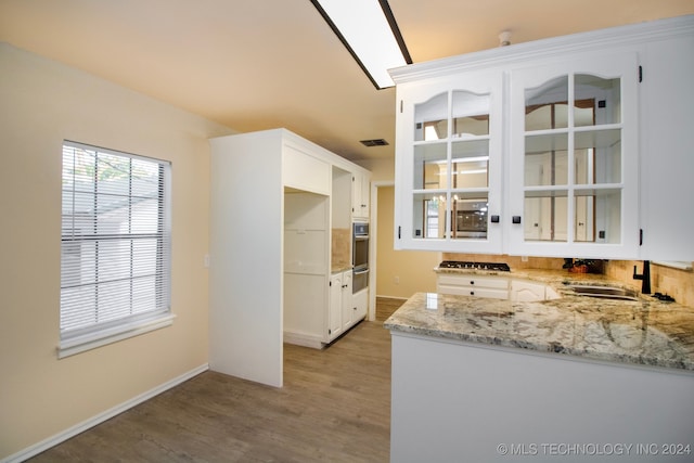 kitchen featuring visible vents, light stone countertops, oven, light wood-style floors, and a sink
