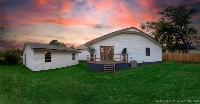 back house at dusk with a deck, a lawn, and central AC unit